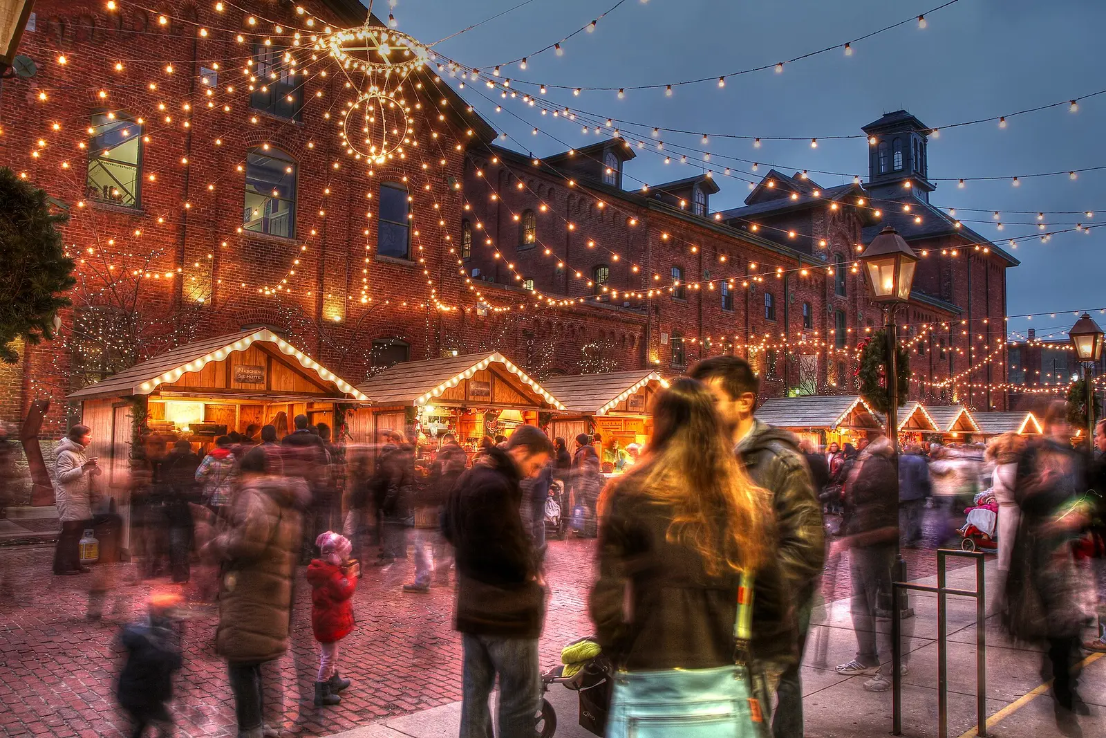 Crowds among lit wooden stalls at the Distillery District Christmas Market at dusk